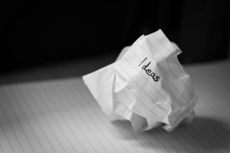 Zerknülltes Blatt Papier mit dem Wort „Ideas“ auf einem Notizblock
